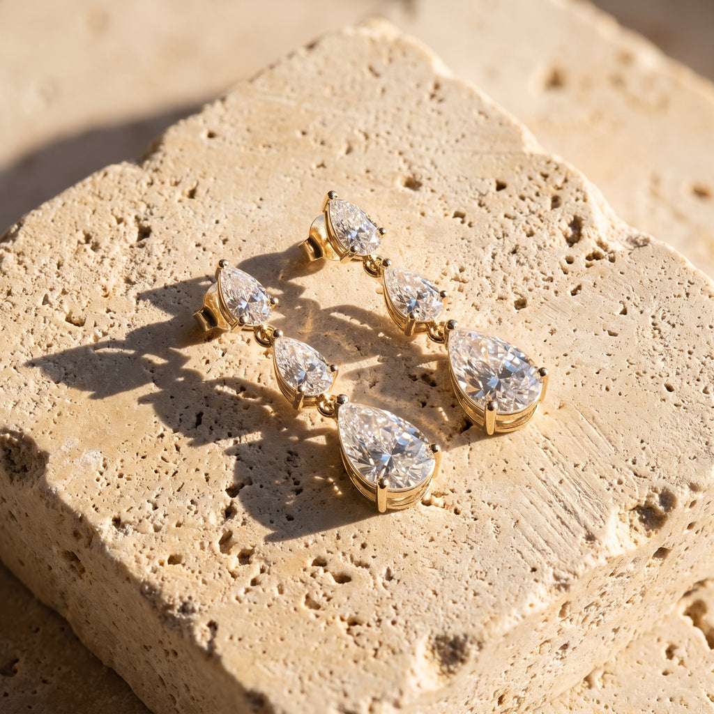 Leah's Ascent graduated pear diamond drop earrings in 14k gold, resting on Jerusalem stone in late afternoon light