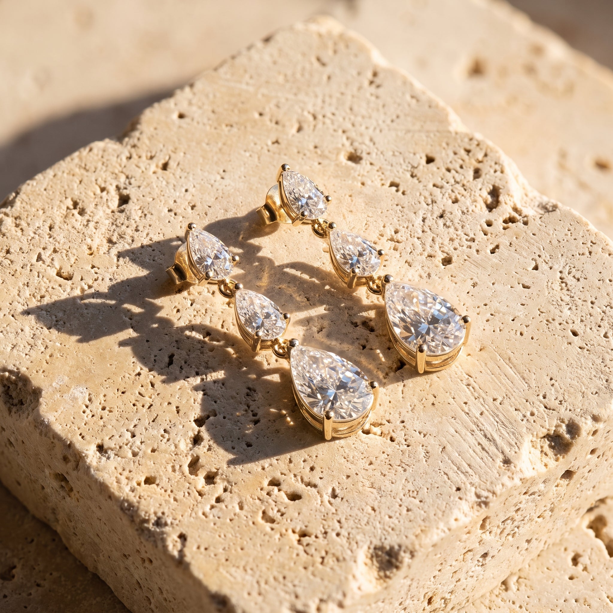 Leah's Ascent graduated pear diamond drop earrings in 14k gold, resting on Jerusalem stone in late afternoon light