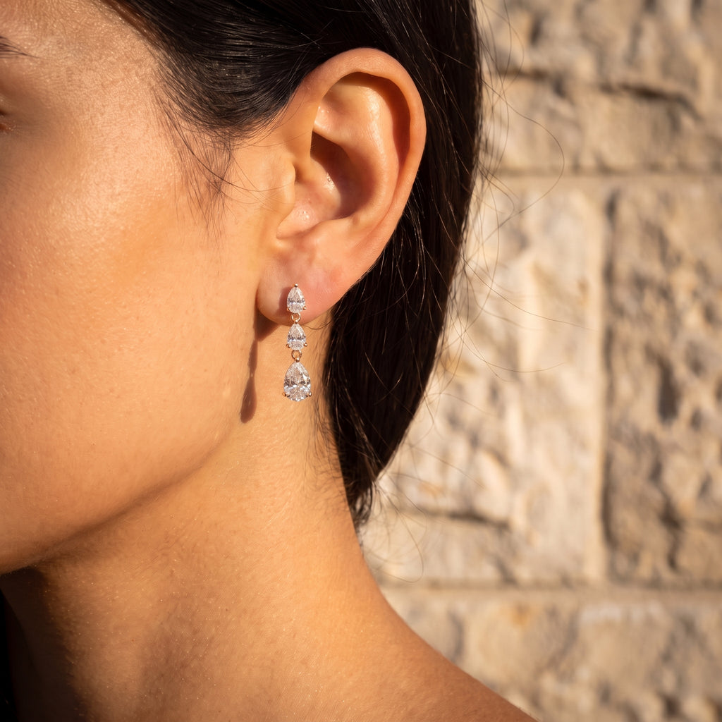 Leah's Ascent worn at the ear, three graduating pear diamonds falling from the lobe against a stone wall
