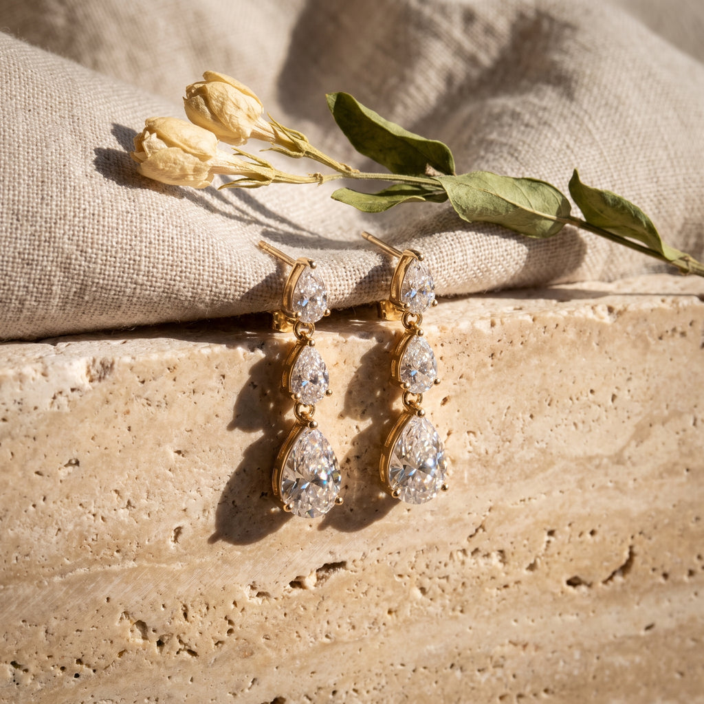 The pair of Leah's Ascent earrings laid on travertine and raw linen beside a dried flowering branch