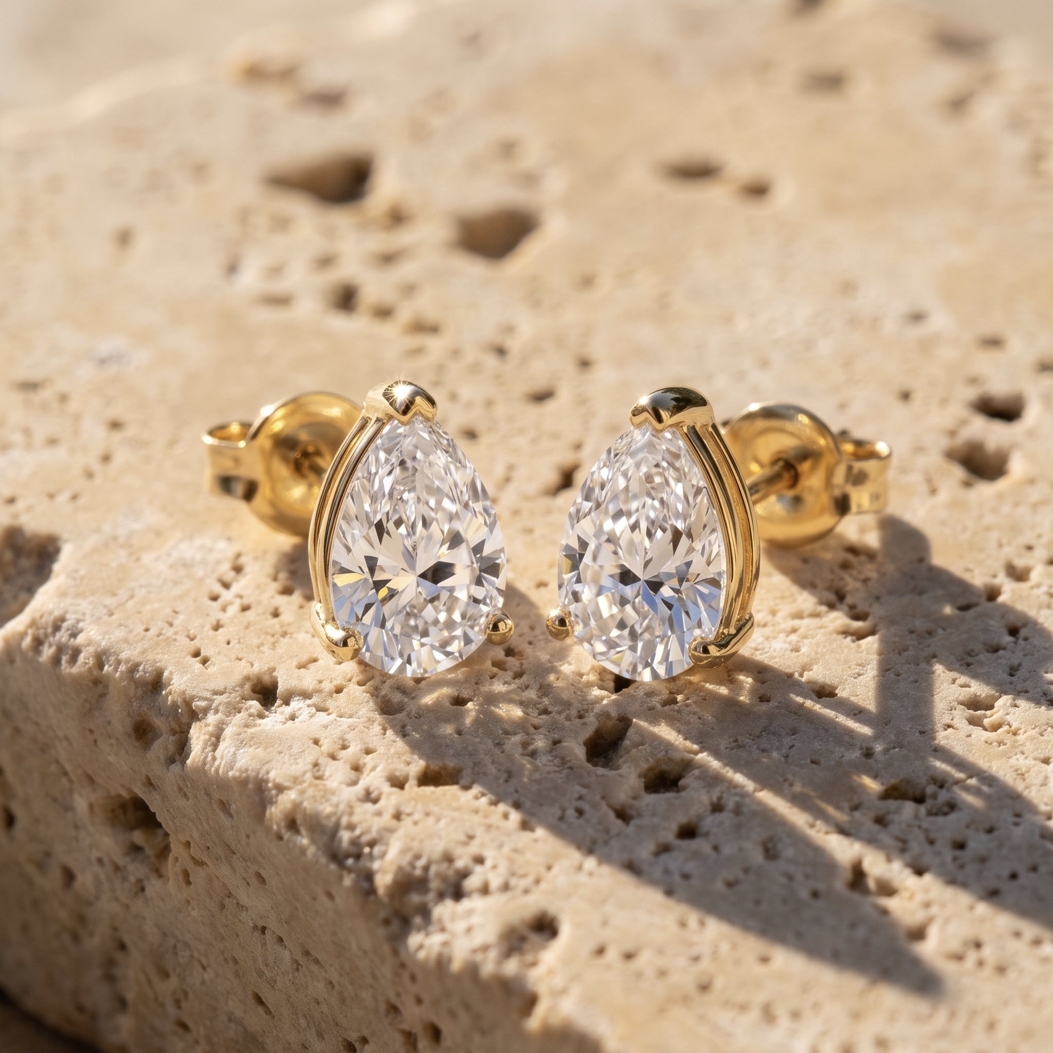 Leah's Tear pear-cut solitaire studs in 14k yellow gold, three-prong setting, on raw Jerusalem stone