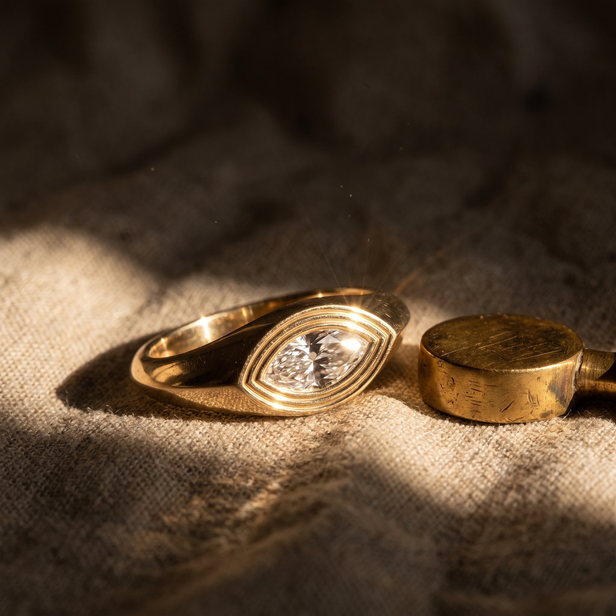 Leah's Whisper signet ring on raw linen beside an aged brass seal in late golden-hour light