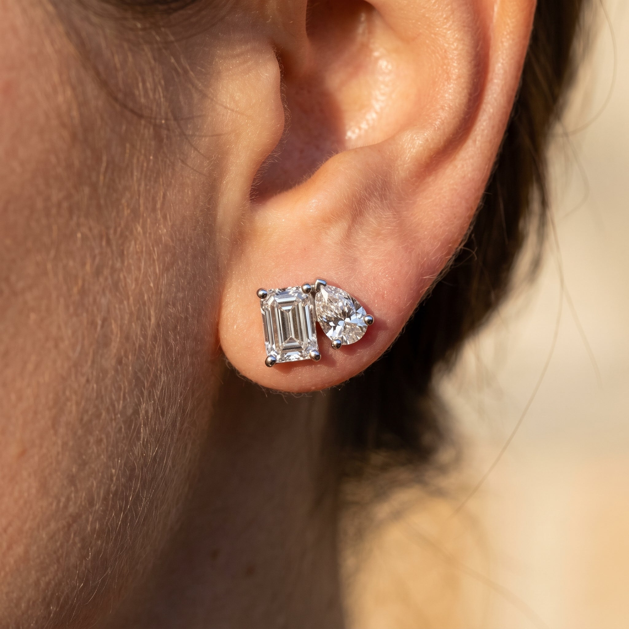 Toi et moi diamond stud earring worn on the ear, emerald and pear cut in 14k white gold