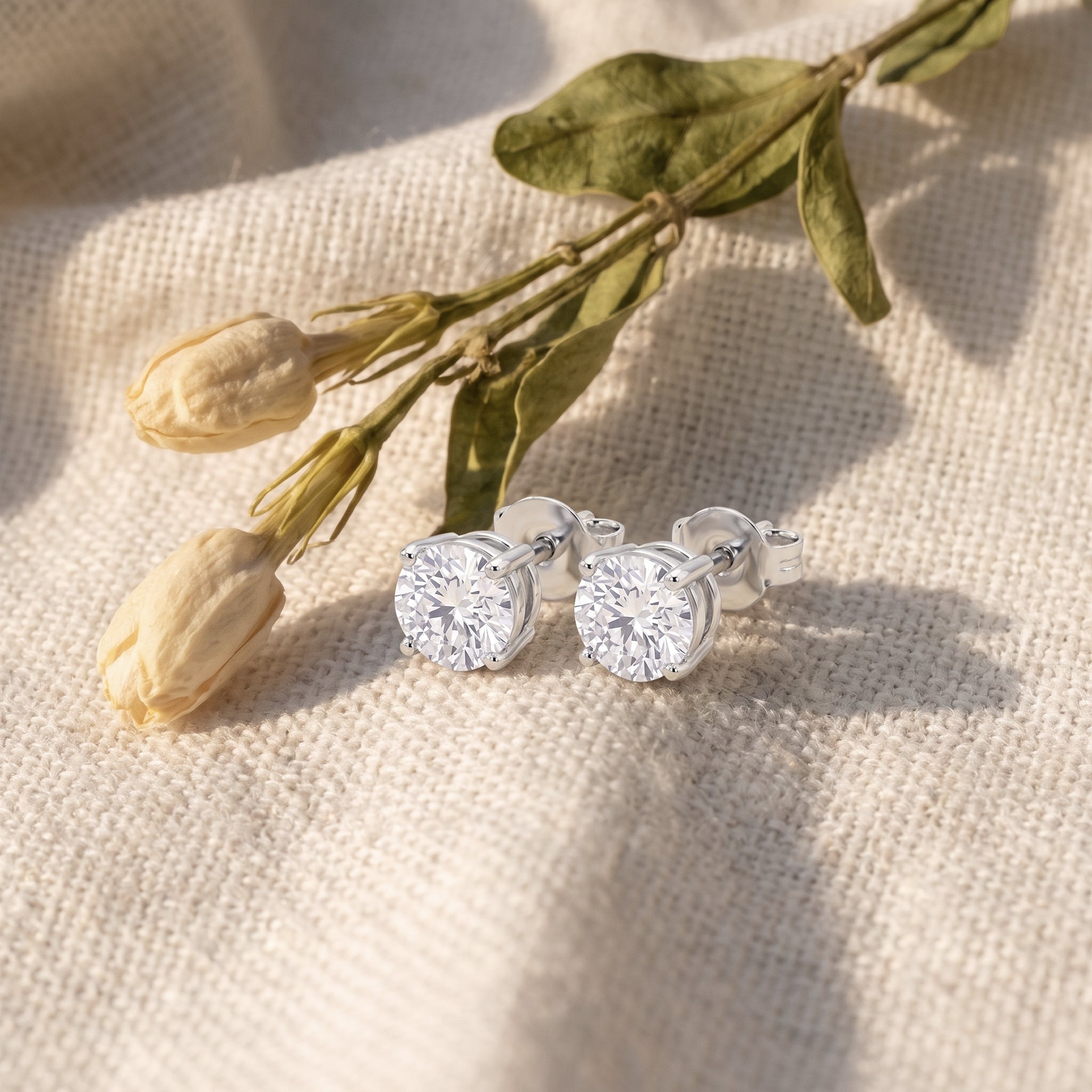 Sarah's Light diamond studs on oatmeal linen with dried tulip buds and olive leaves