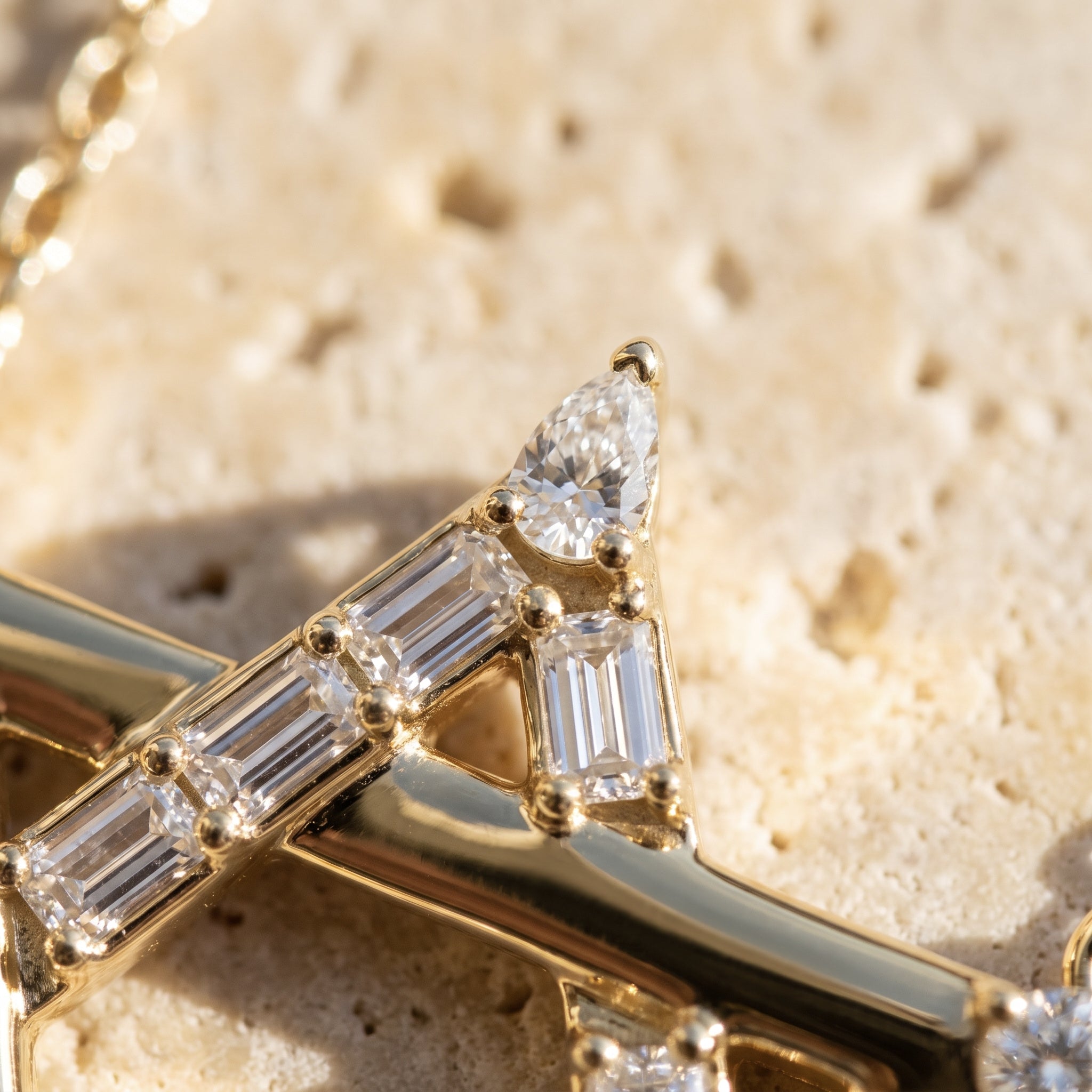Macro detail of Sarah's Shield: pear-cut diamond tip and channel-set baguettes on the polished 14k yellow gold bar
